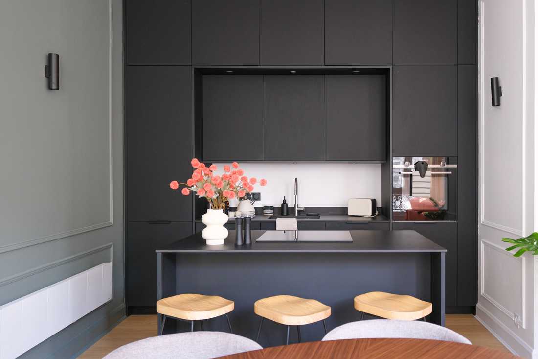 Cuisine ouverte noire mate avec îlot central et tabouret design avec assise en bois